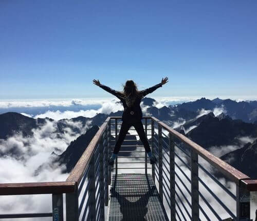 Person freut sich am Gipfel mit Bergausblick. Eine Analogie zum Erfolg im Studium mit Zufriedenheit.