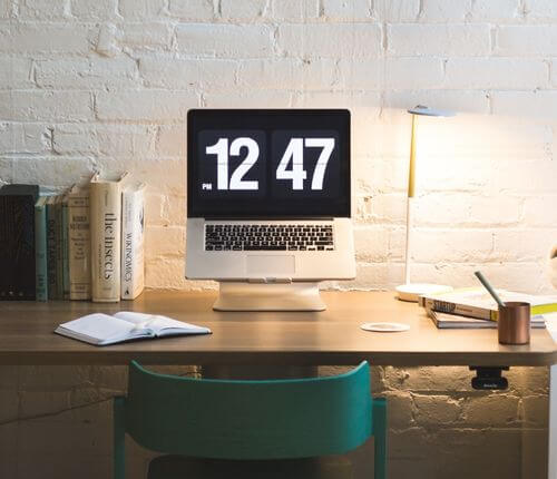 Laptop auf Schreibtisch zeigt groß die laufende Uhr an. Die Zeit im Studium rennt.
